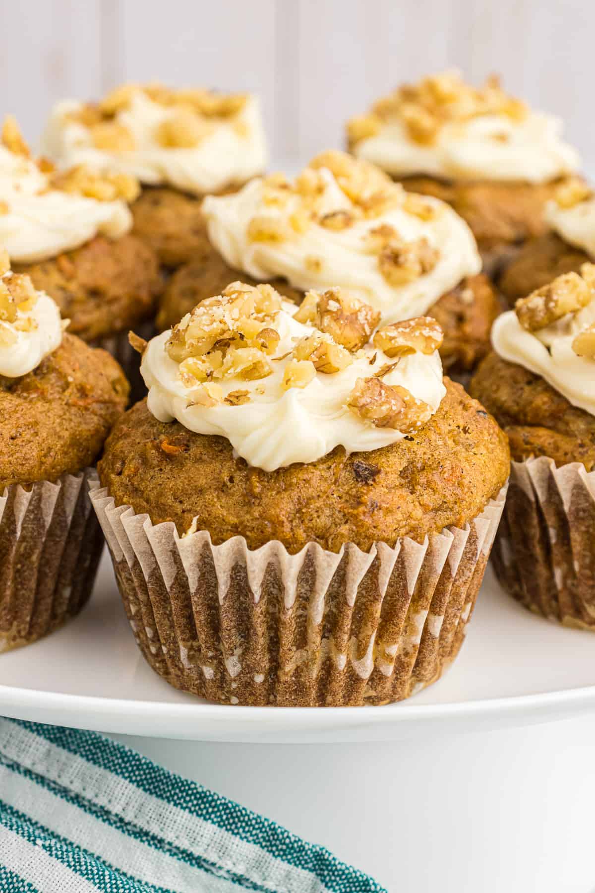 Carrot cake muffins on a white plate topped with cream cheese frosting and chopped walnuts.