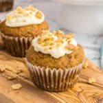 Two carrot cake muffins on a wood board.