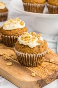 Two carrot cake muffins on a wood board.