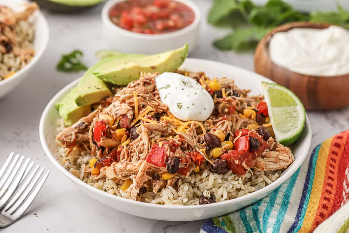 Shredded chicken with black beans and red bell pepper over rice in a white bowl next to a colorful kitchen cloth.