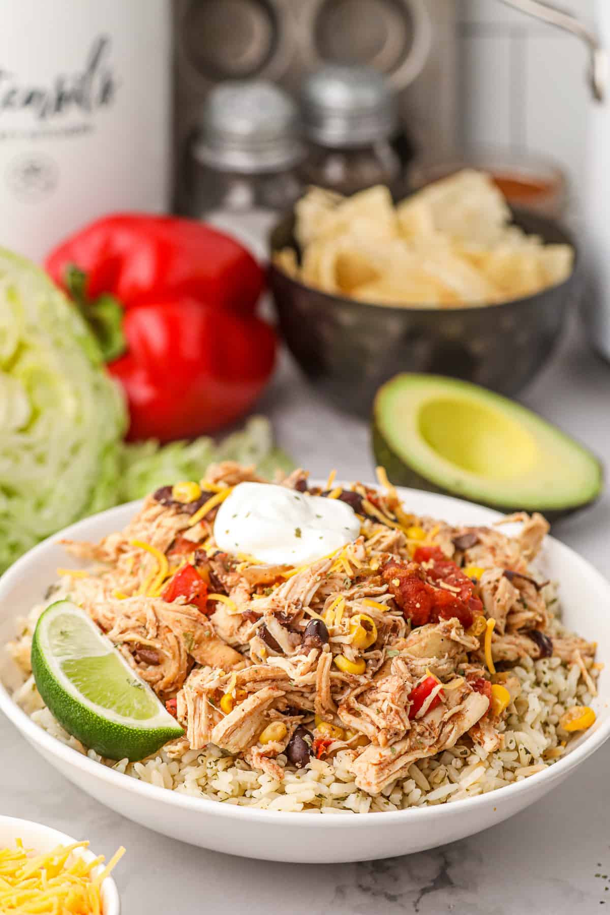 Shredded Tex-Mex Chicken on rice topped with sour cream in a white bowl with a lime wedge.