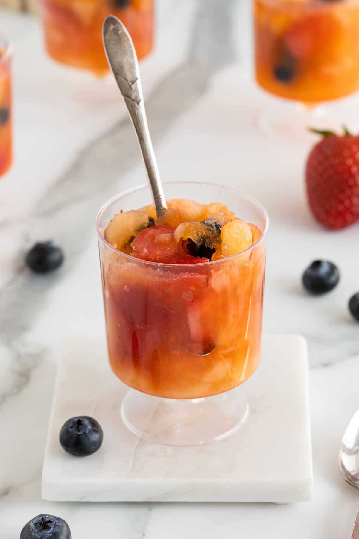 A spoon stuck into a plastic cup of slushy frozen fruit.