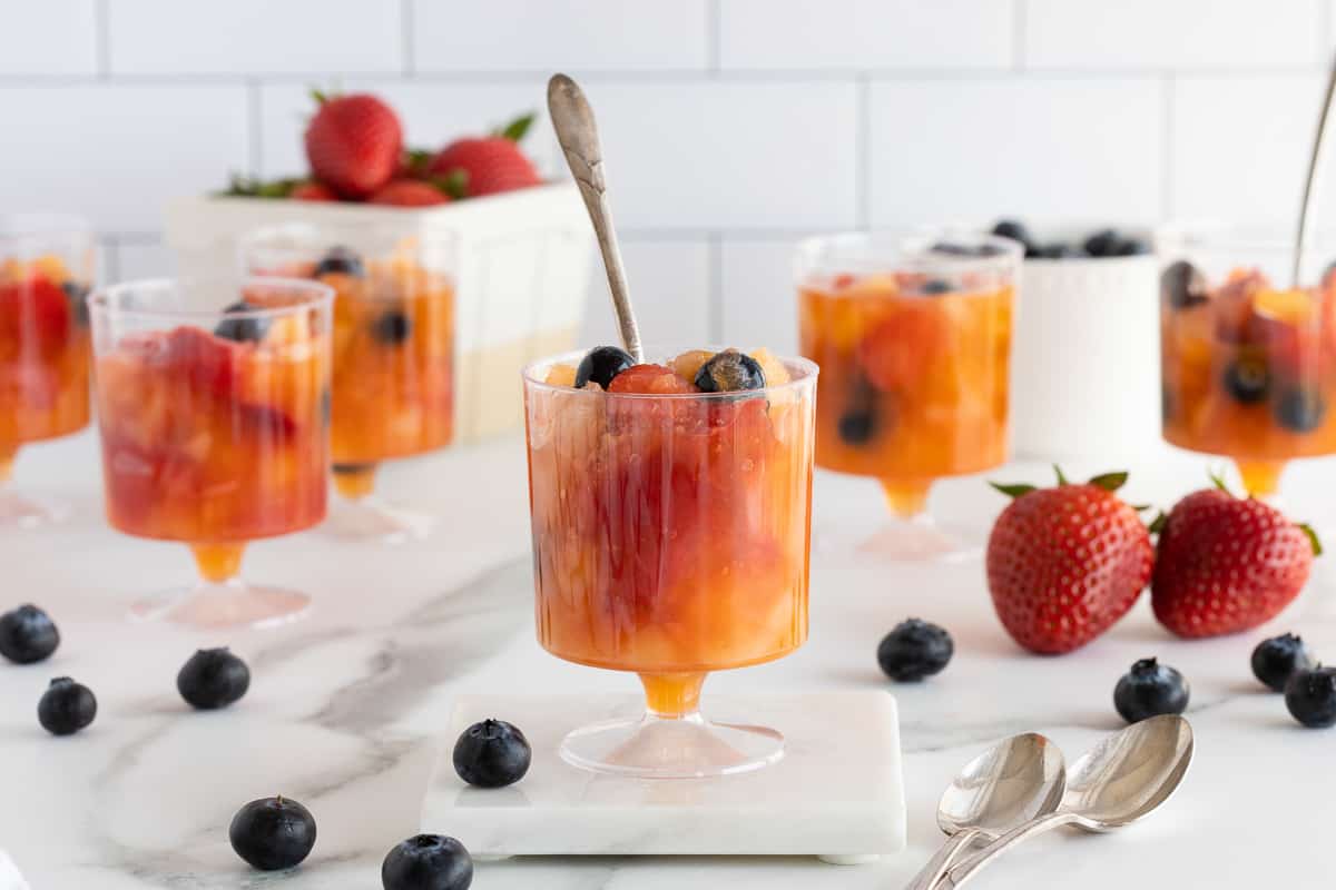 Plastic cups filled with frozen fruit surrounded by blueberries and strawberries.