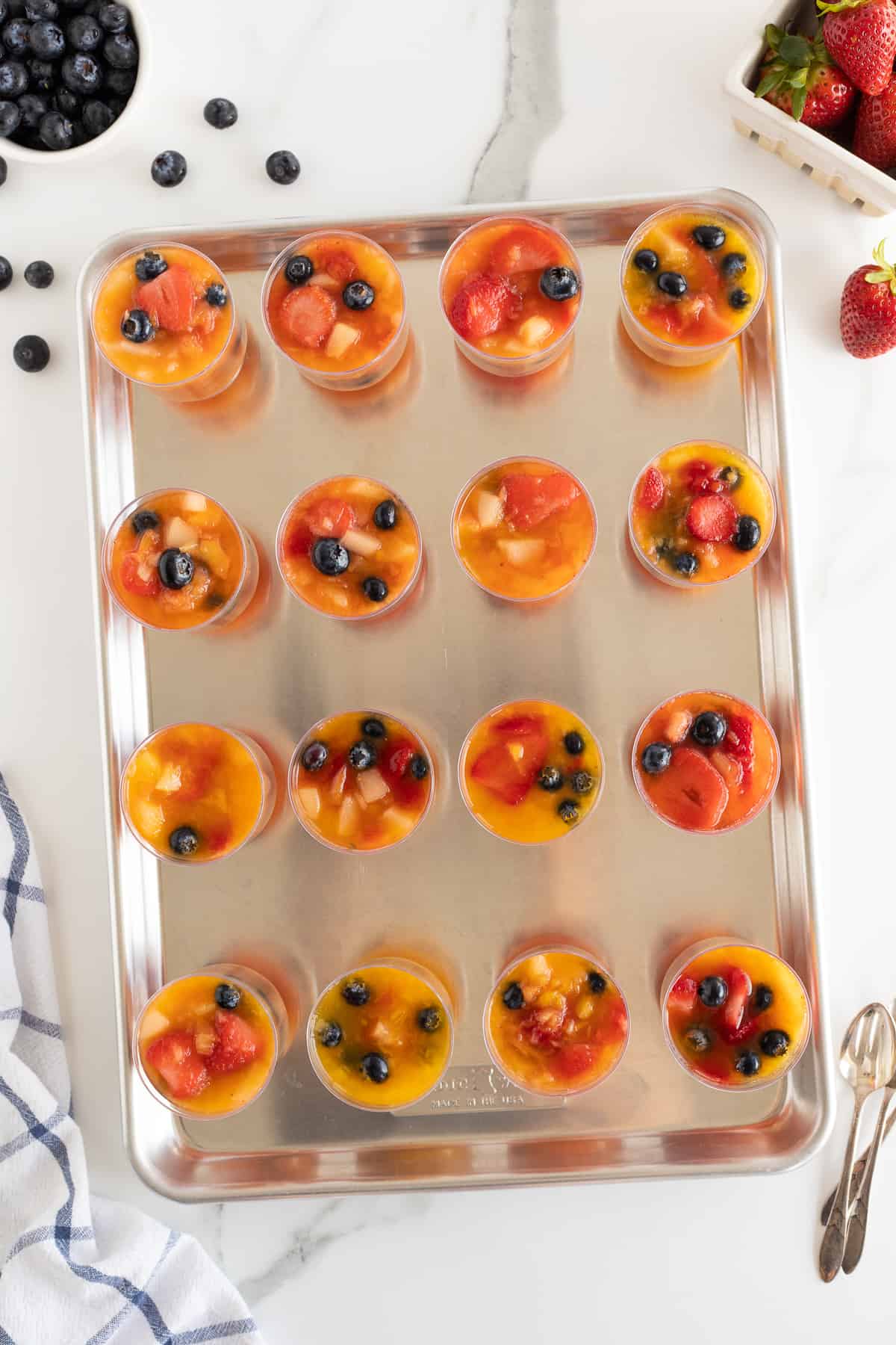 A top down shot of plastic cups filled with frozen fruit on a baking sheet.