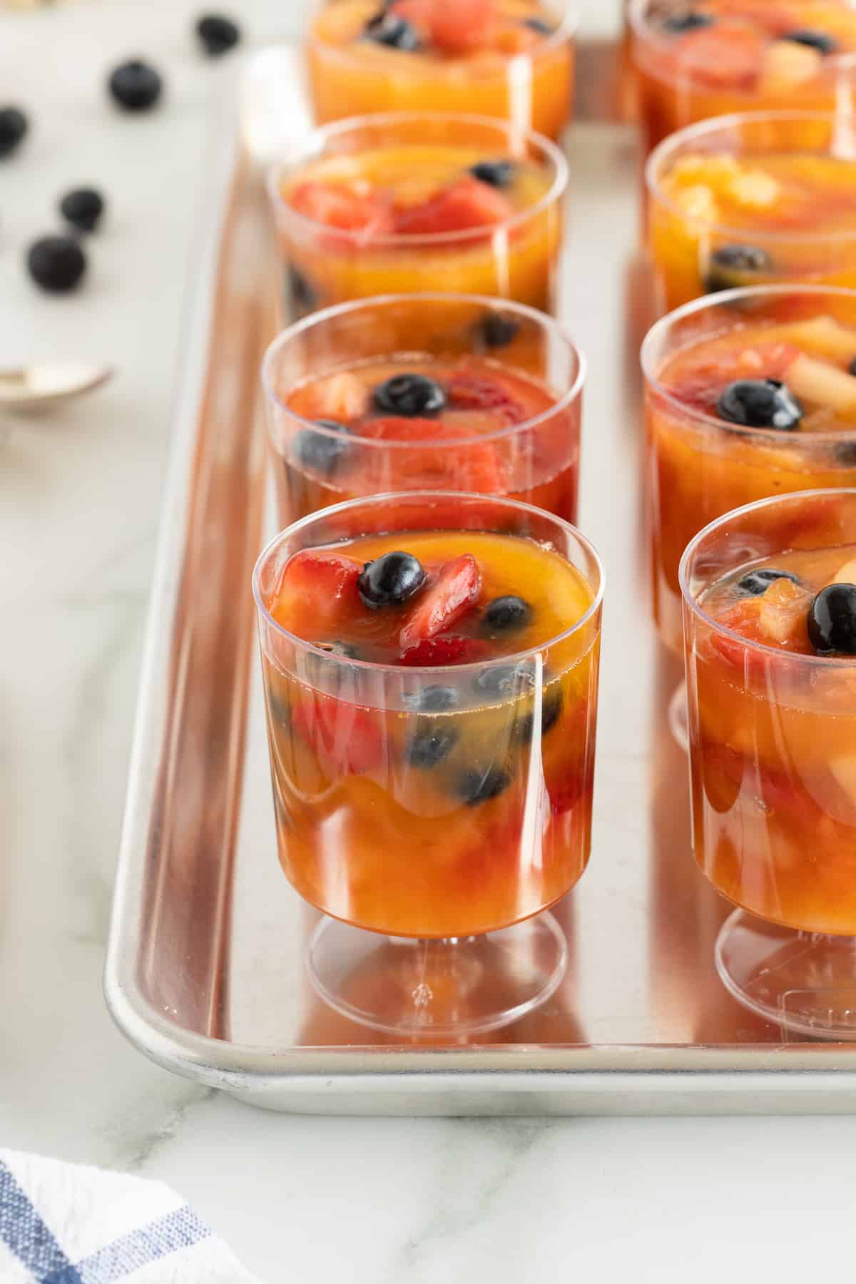 A close up of plastic cups filled with frozen fruit on a baking sheet.