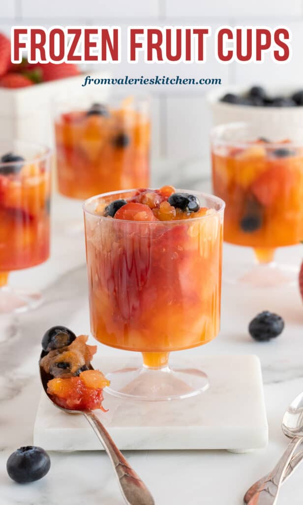 A spoon resting near plastic cups filled with slushy frozen fruit with text.