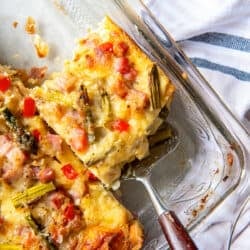 A top down shot of a spatula resting under a slice of breakfast strata in a baking dish.