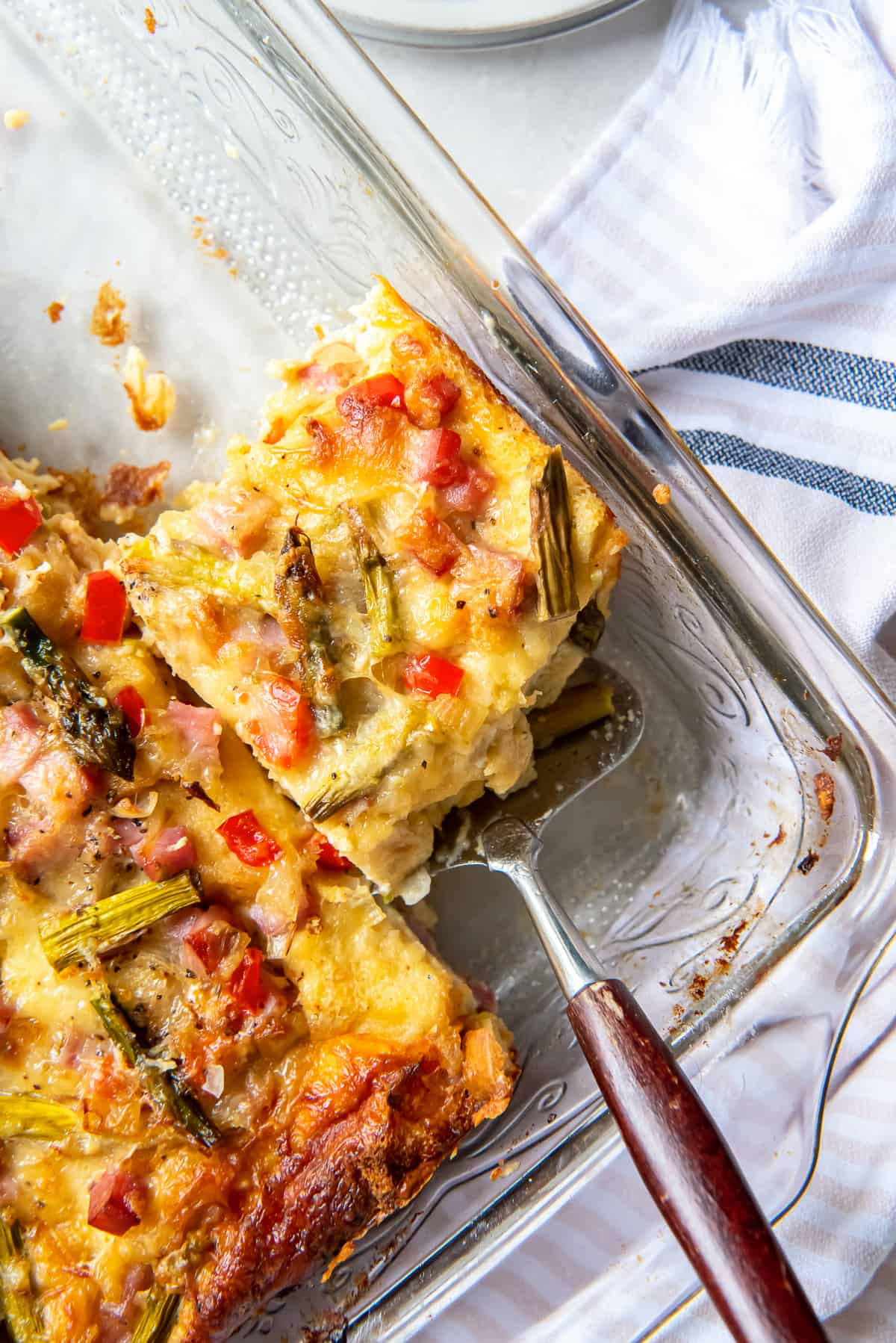 A top down shot of a spatula resting under a slice of breakfast strata in a baking dish.