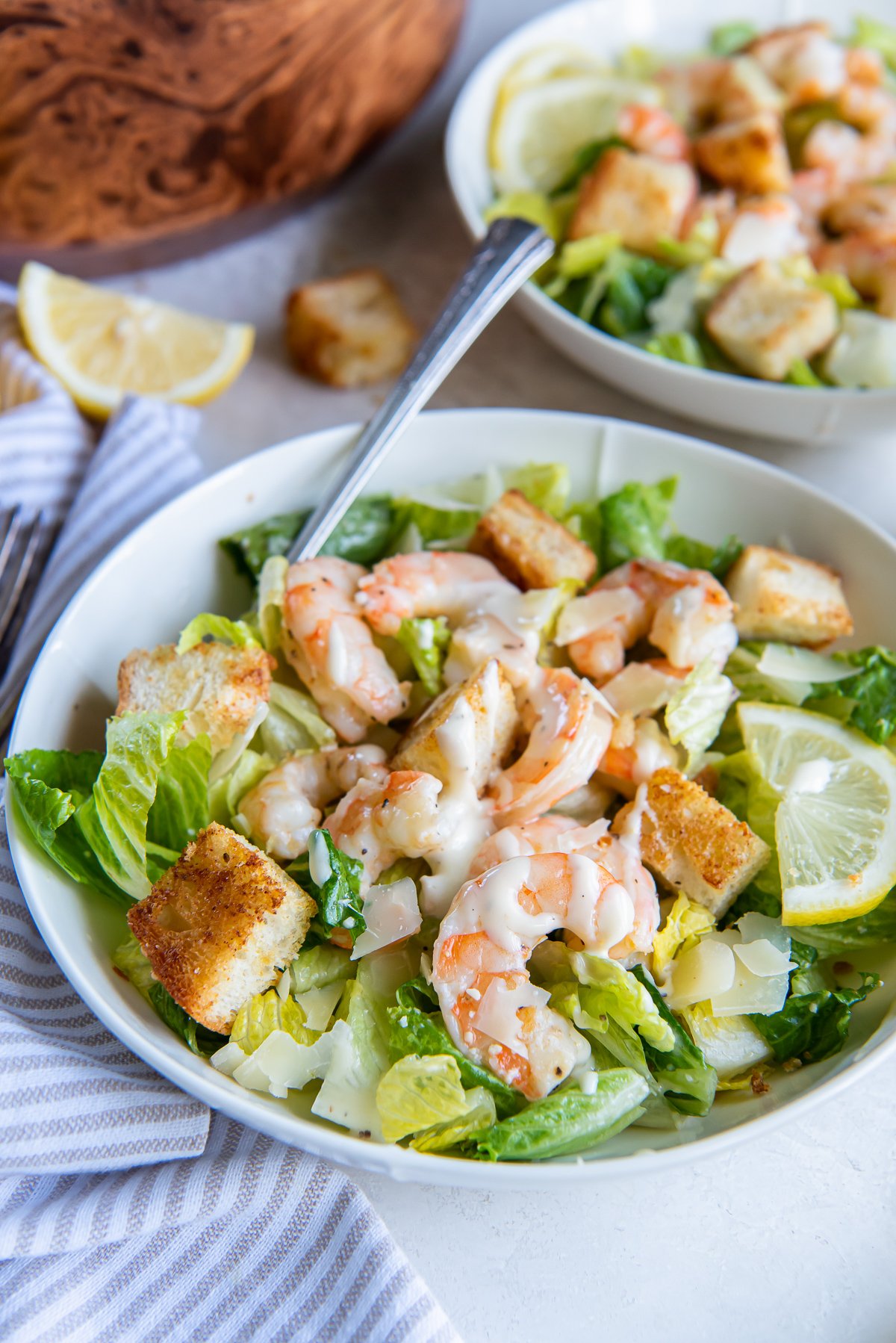 A fork resting in a bowl with caesar salad with shrimp and, croutons, and dressing.