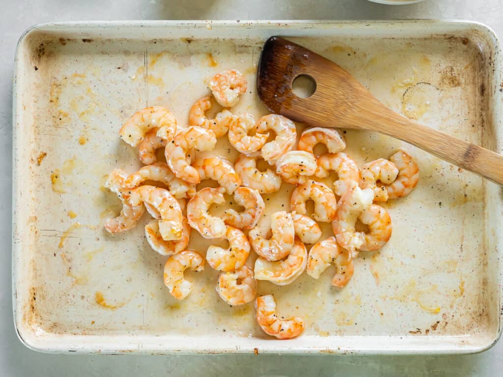 Roasted shrimp on a baking sheet with a wooden spatula.