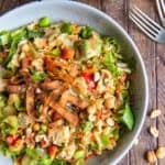 A top down shot of a salad with chicken, edamame, peanut dressing and wonton strips next to a carafe of dressing and forks.