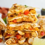Wedges of chicken fajita quesadillas stacked on a white plate with a lime wedge.