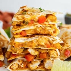 Wedges of chicken fajita quesadillas stacked on a white plate with a lime wedge.