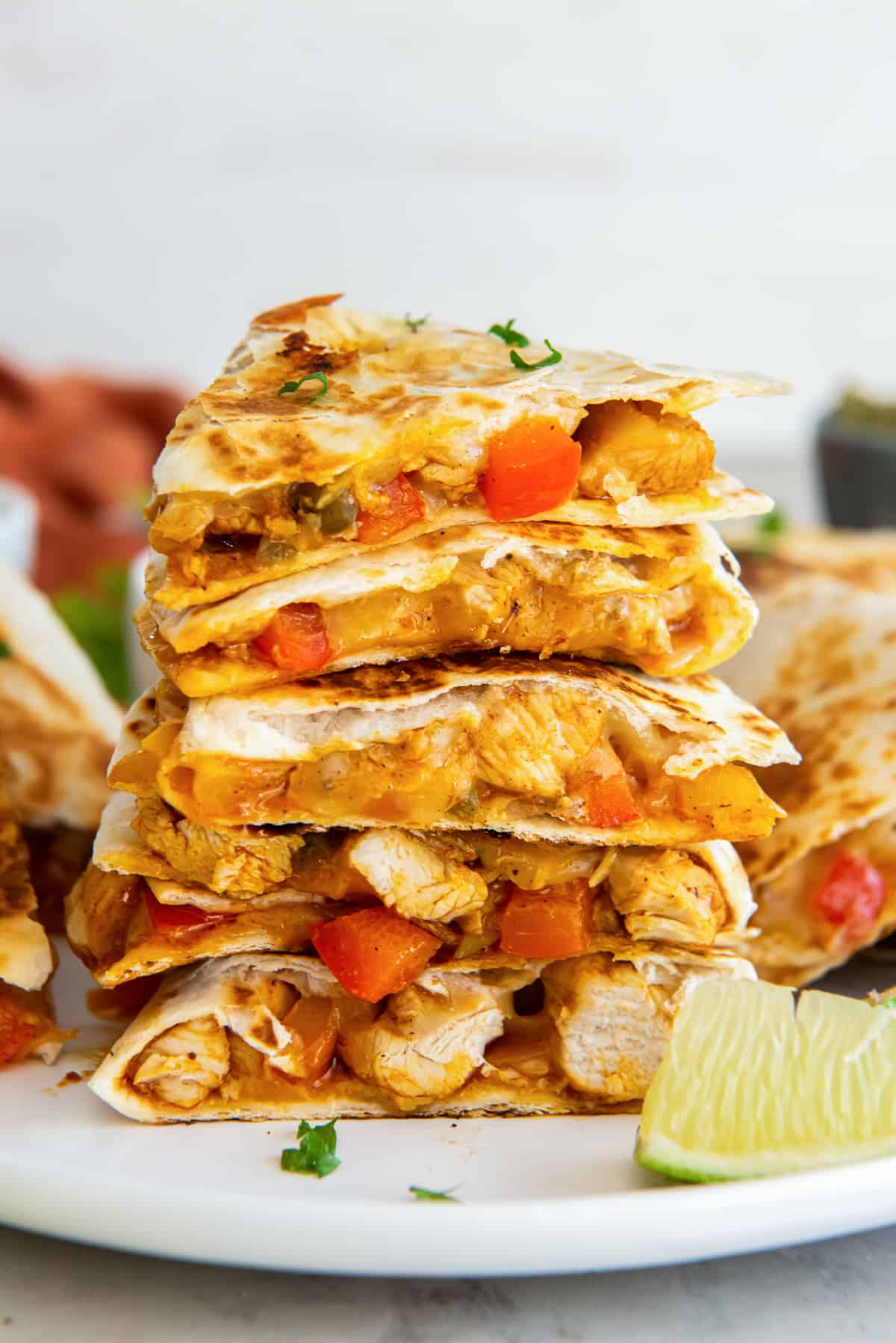 Wedges of chicken fajita quesadillas stacked on a white plate with a lime wedge.