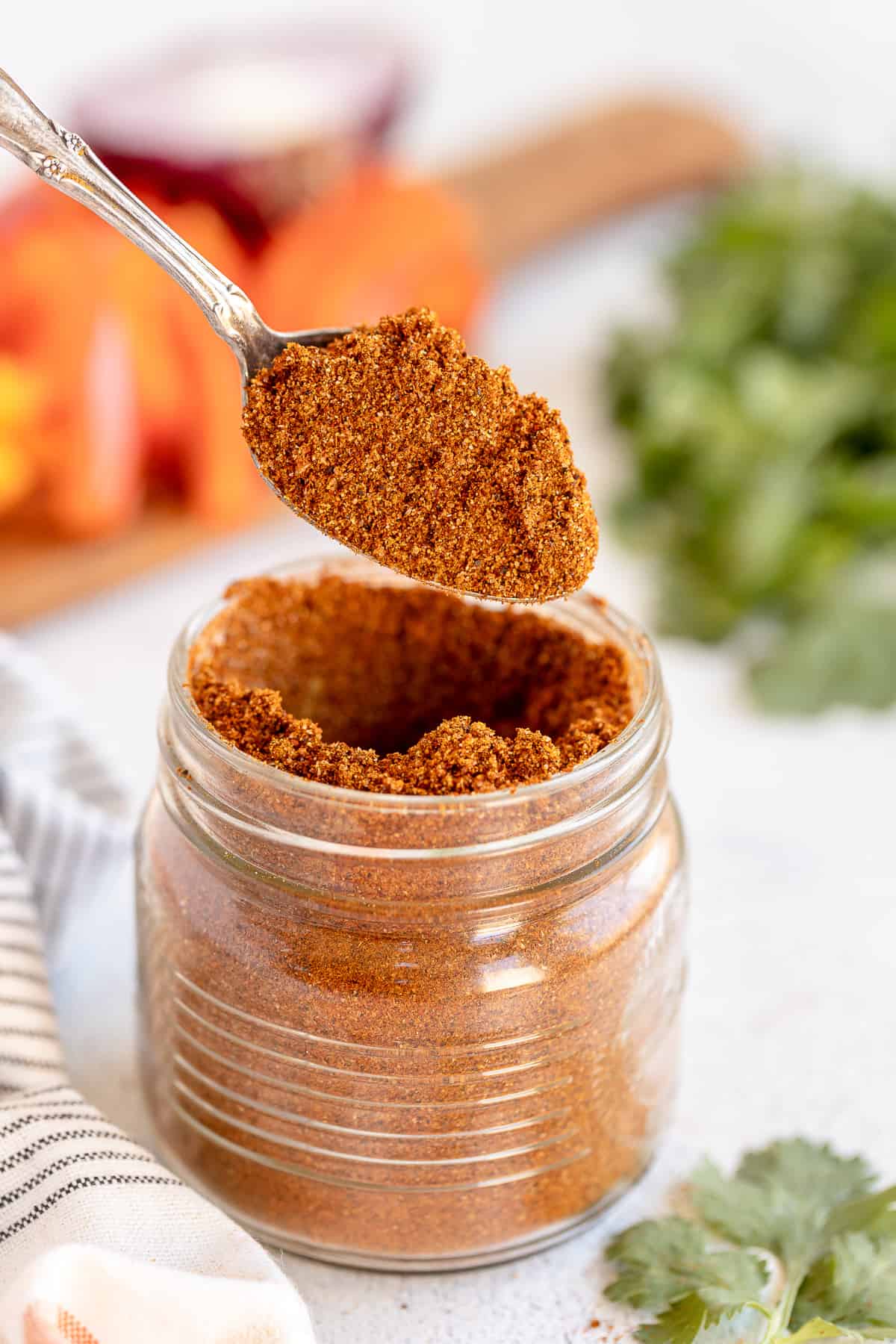 A spoon lifts fajita seasoning from a mason jar.