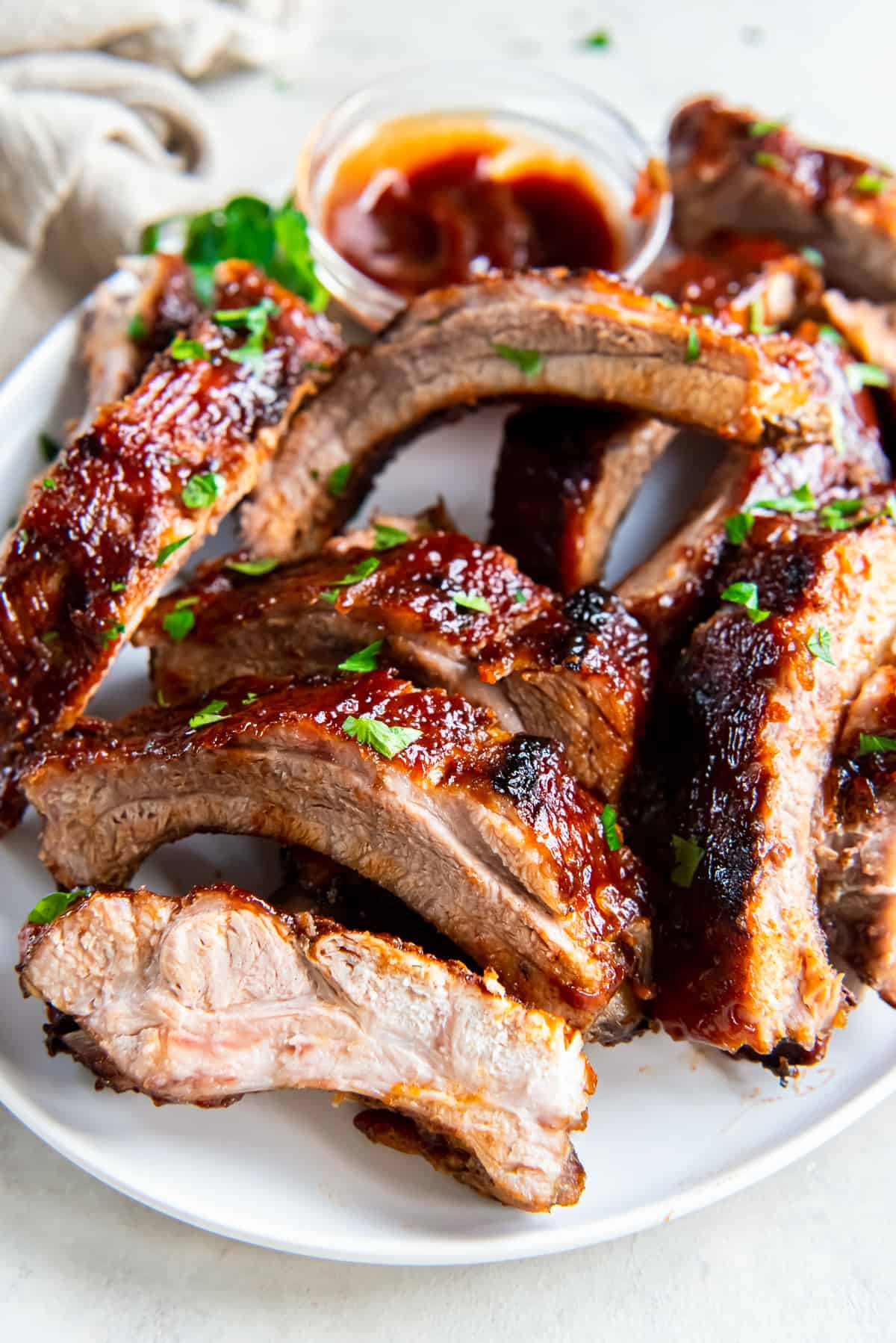 Baby back ribs with BBQ sauce piled on a white platter.