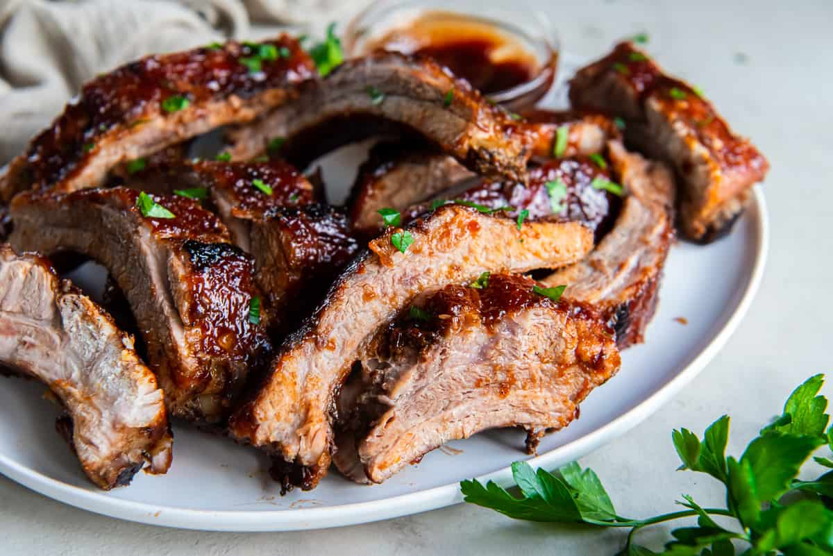 Baby back ribs with BBQ sauce piled on a white platter.