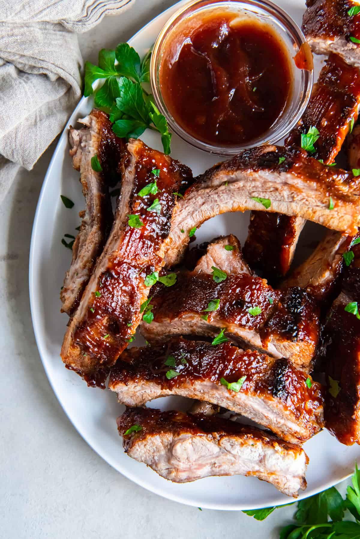 Baby back ribs with BBQ sauce piled on a white platter.