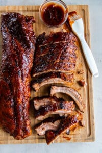 Two racks of baby back ribs on a wood cutting board with bbq sauce and a pastry brush.