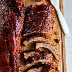 Two racks of baby back ribs on a wood cutting board with bbq sauce and a pastry brush.