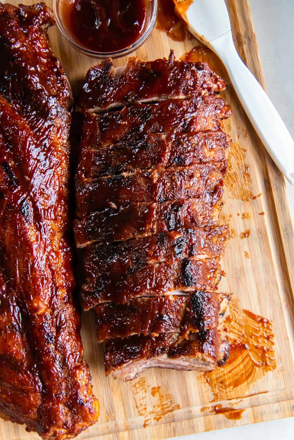 Two racks of baby back ribs on a wood cutting board with bbq sauce and a pastry brush.