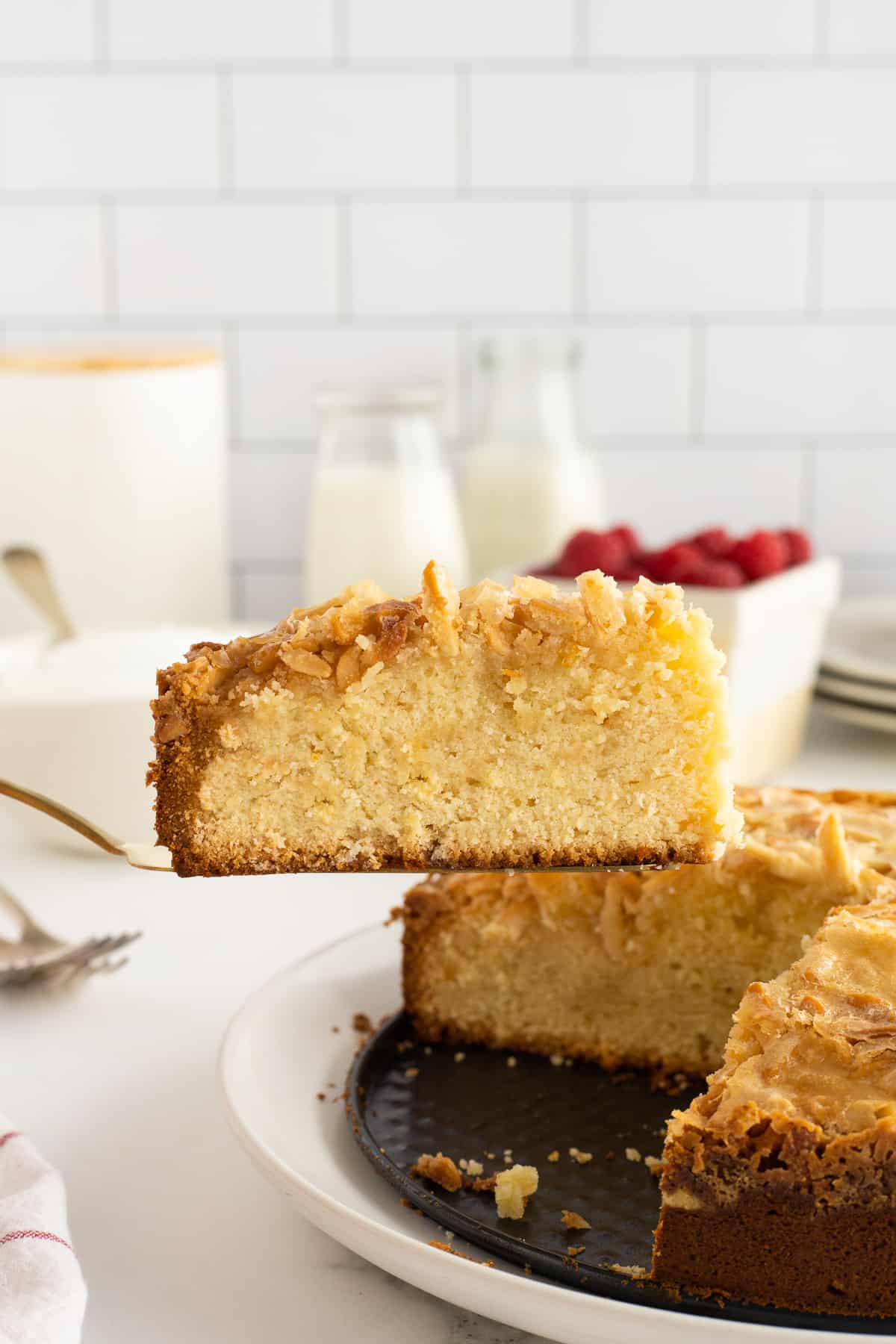 A spatula lifting a slice of almond pound cake from a platter.