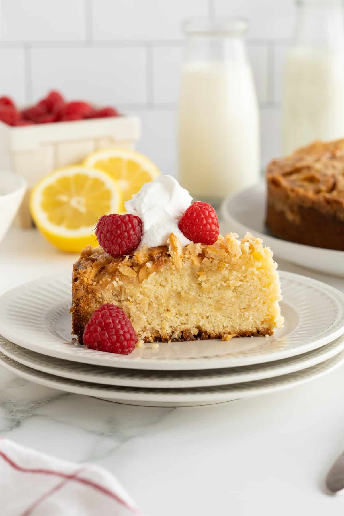 A slice of almond pound cake topped with whipped cream and raspberries on a white plate.