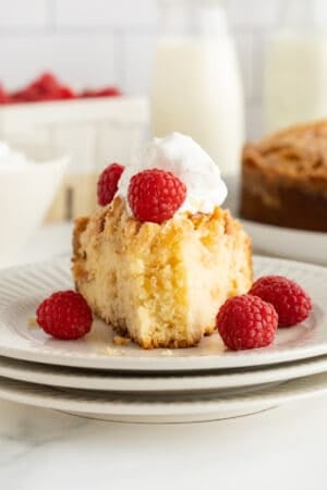 A slice of almond pound cake topped with whipped cream and raspberries with a bite missing on a white plate.