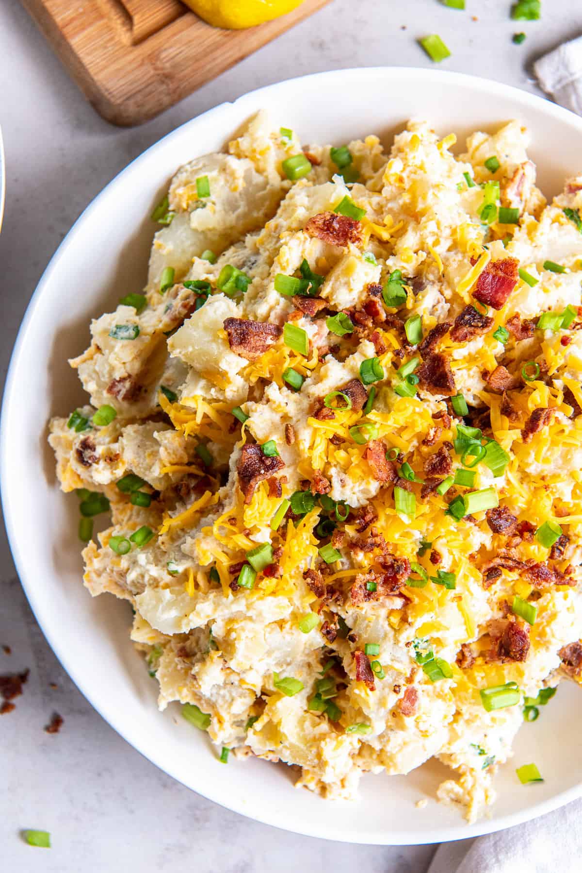 A top down shot of a bowl of potato salad with cheese, bacon and green onions.