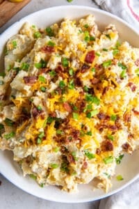 A top down shot of a bowl of potato salad with cheese, bacon, and green onions.