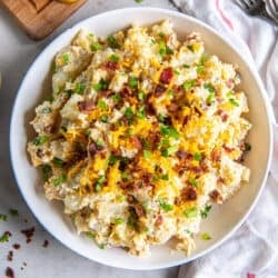 A top down shot of a bowl of potato salad with cheese, bacon, and green onions.