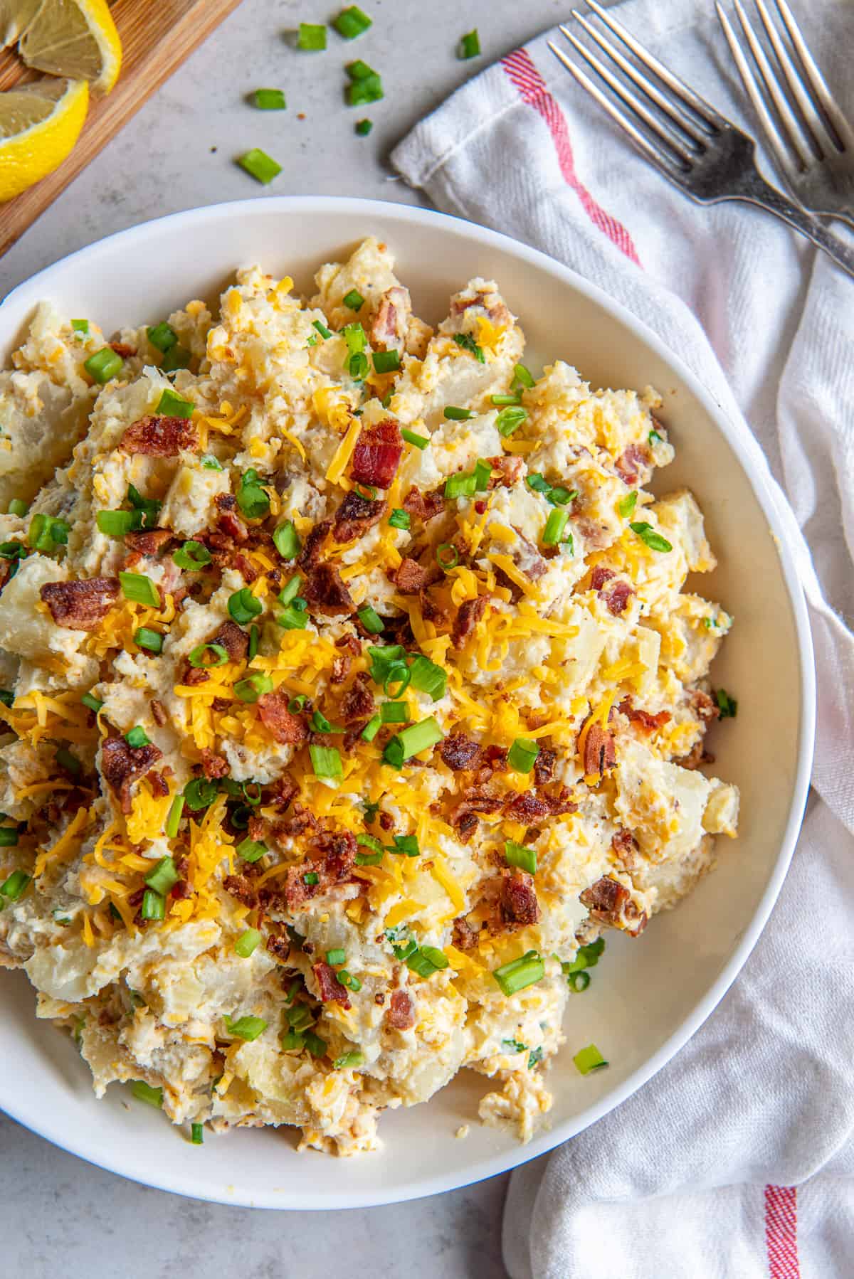 A top down shot of a bowl of potato salad with cheese, bacon, and green onions.