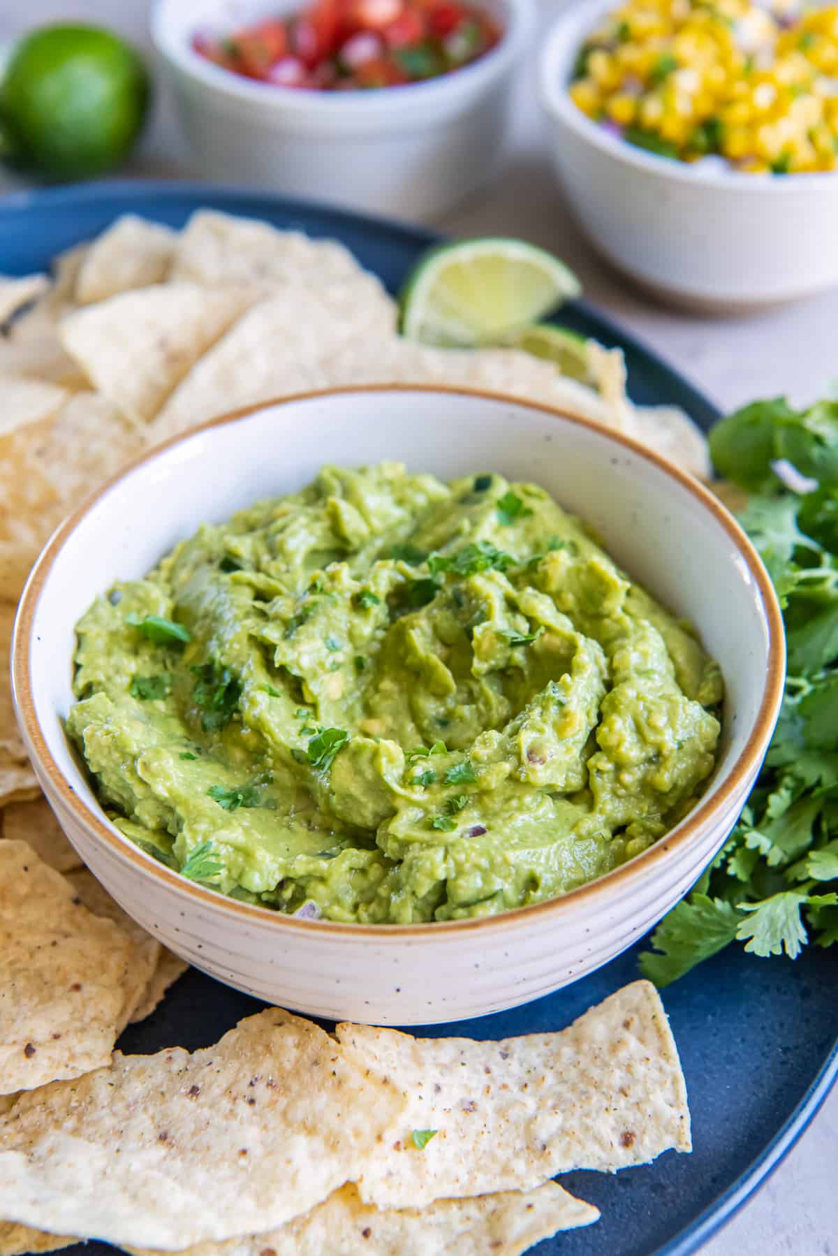 A white bowl filled with guacamole on a platter with cilantro and tortilla chips.