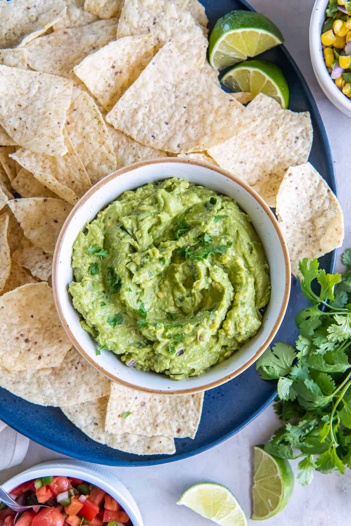 A top down shot of a bowl of guacamole on a platter with tortilla chips.