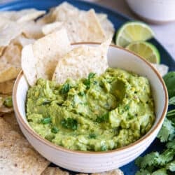 Two tortilla chips pressed into guacamole in a white bowl.