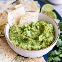 Two tortilla chips pressed into guacamole in a white bowl.