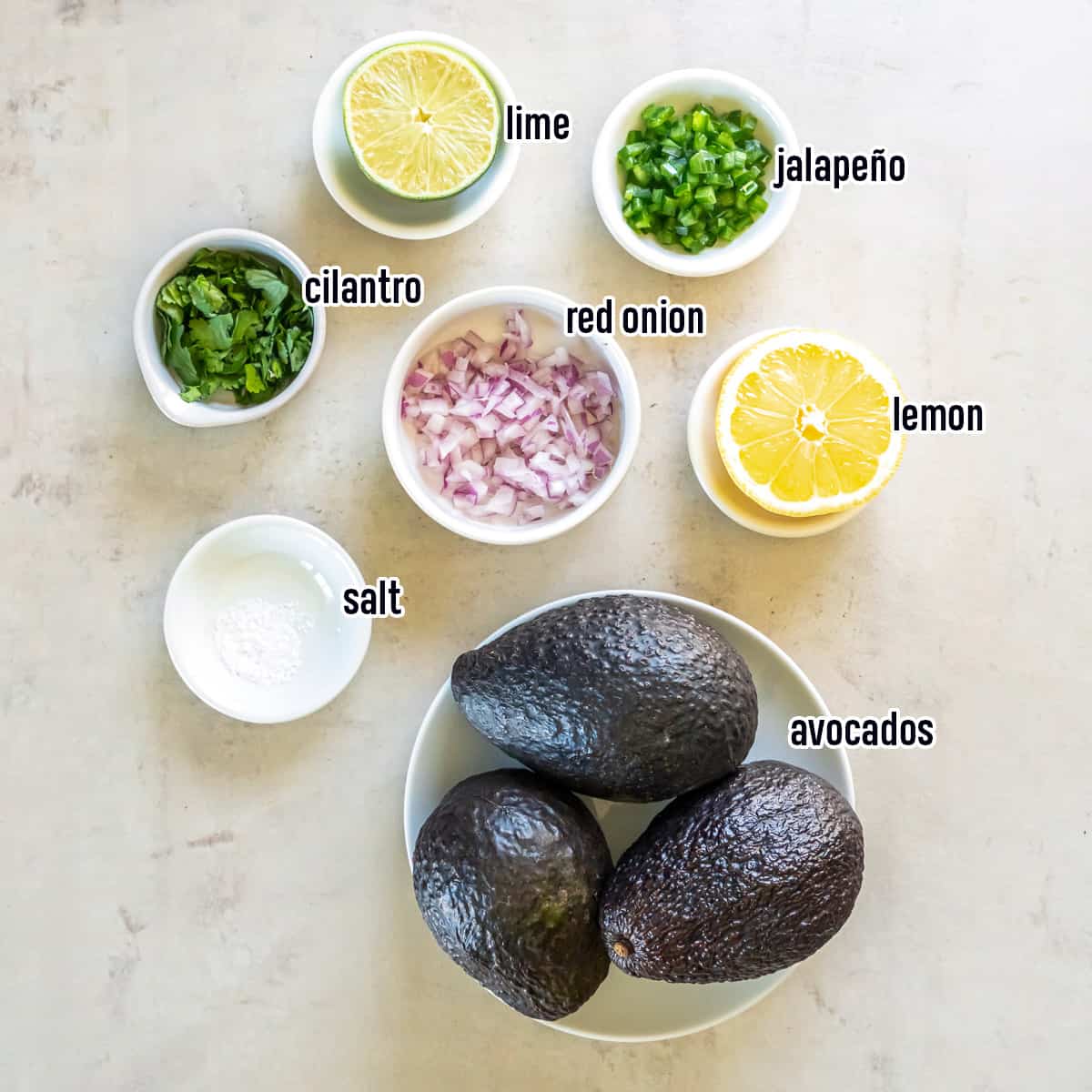 Avocados, diced red onion, jalapeno, and other ingredients for copycat Chipotle Guacamole in bowls with text.