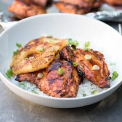 Two pieces of Hawaiian BBQ Chicken with grilled pineapple slices over rice in a white bowl.