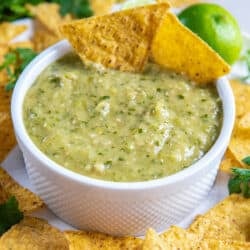 Two tortilla chips resting in a small bowl of tomatillo green salsa.