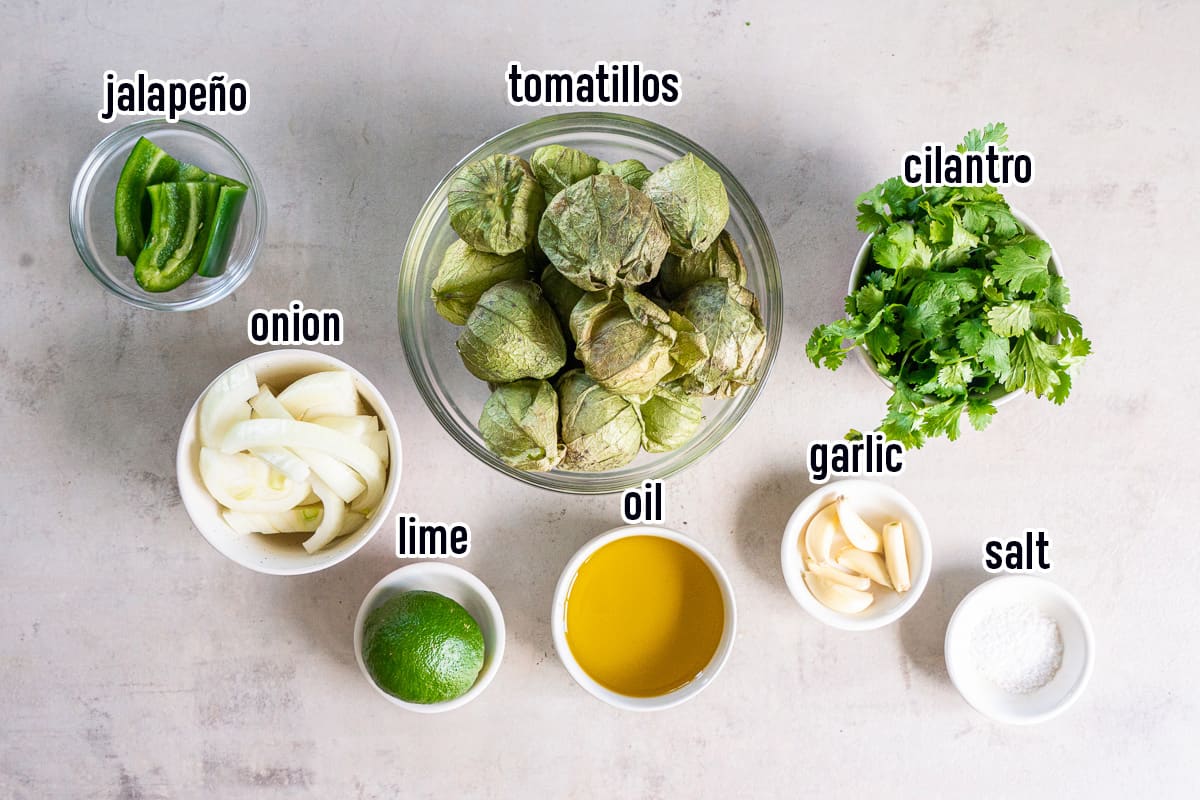 Tomatillos, jalapeno, onion and other ingredients in bowls with text.