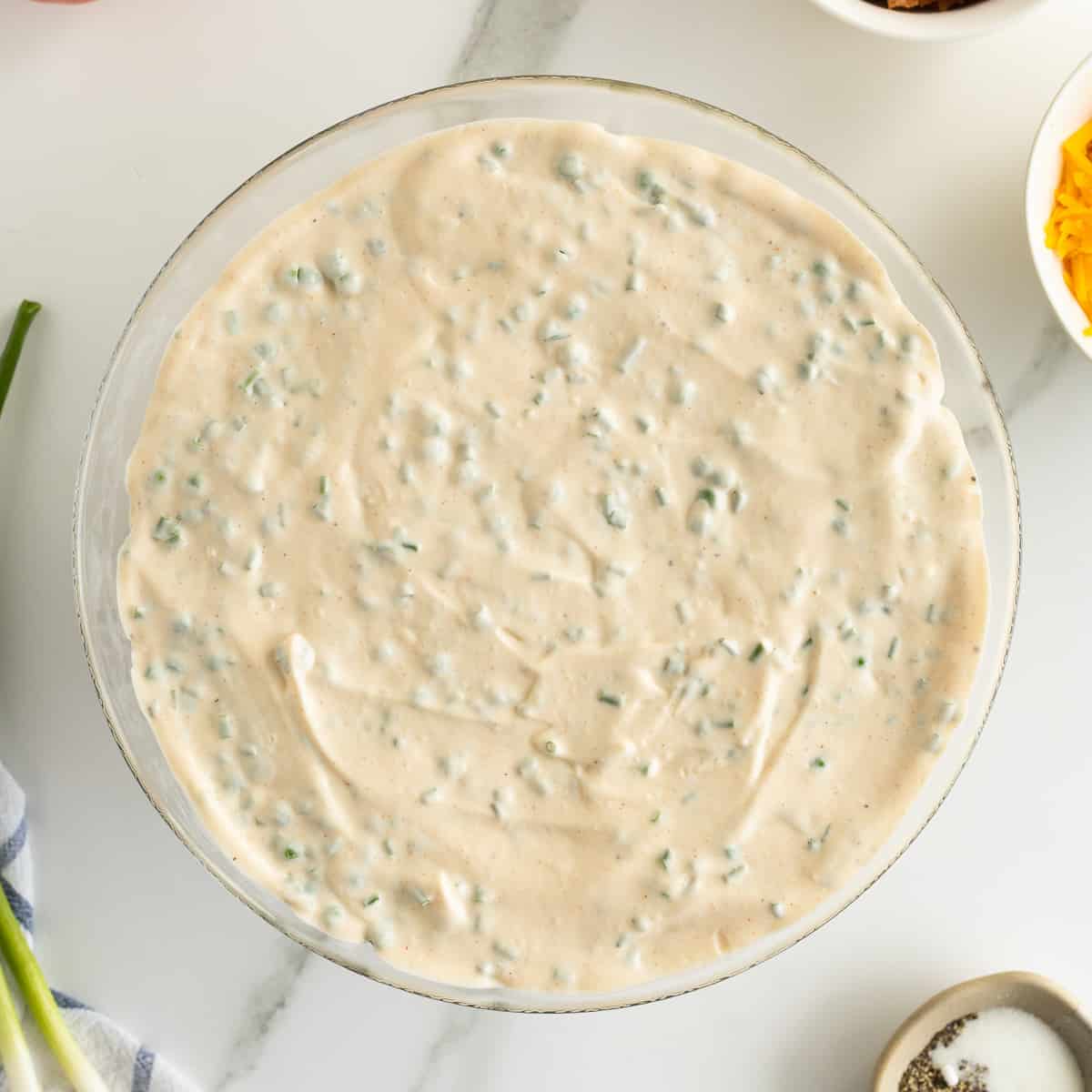 A layer of salad dressing on top of a layered salad in a glass bowl.