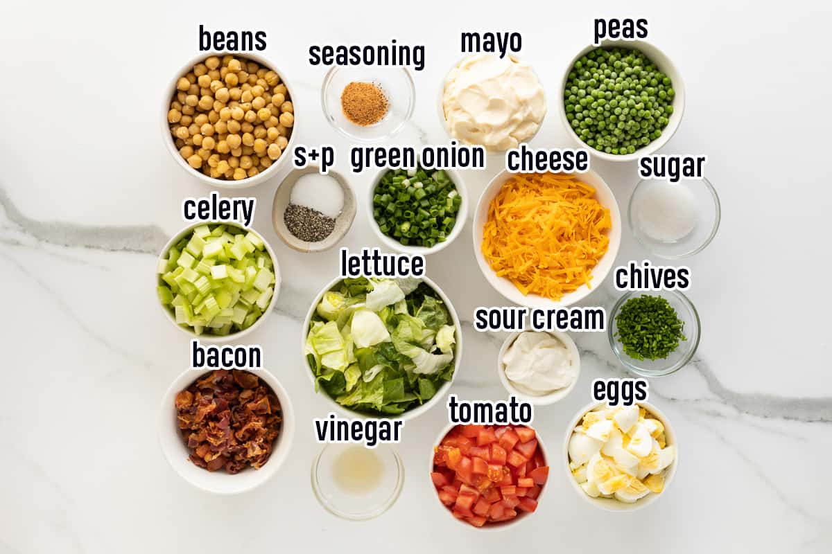 Lettuce, cheese, bacon and other ingredients for layered salad with text.