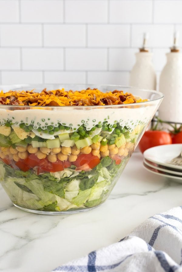 A side view of a glass trifle dish filled with layered salad on a kitchen counter.