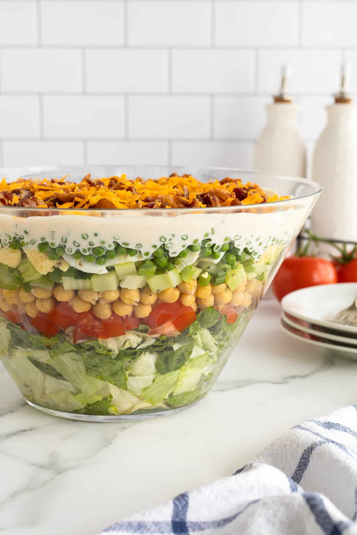 A side view of a glass trifle dish filled with layered salad on a kitchen counter.