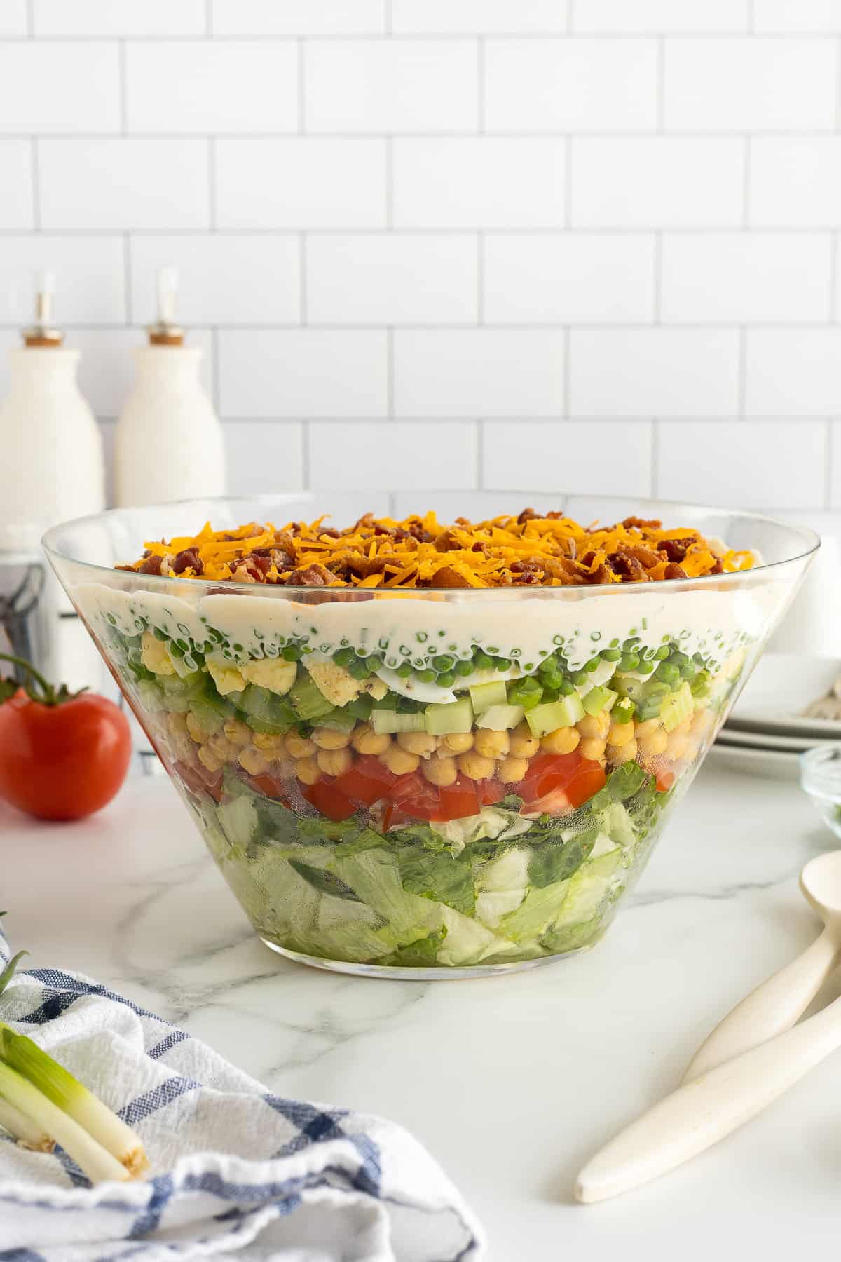 A side view of a glass trifle dish filled with layered salad on a kitchen counter.