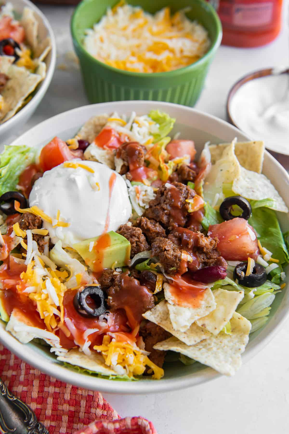 A serving of taco salad in a white bowl topped with sour cream and Catalina dressing.