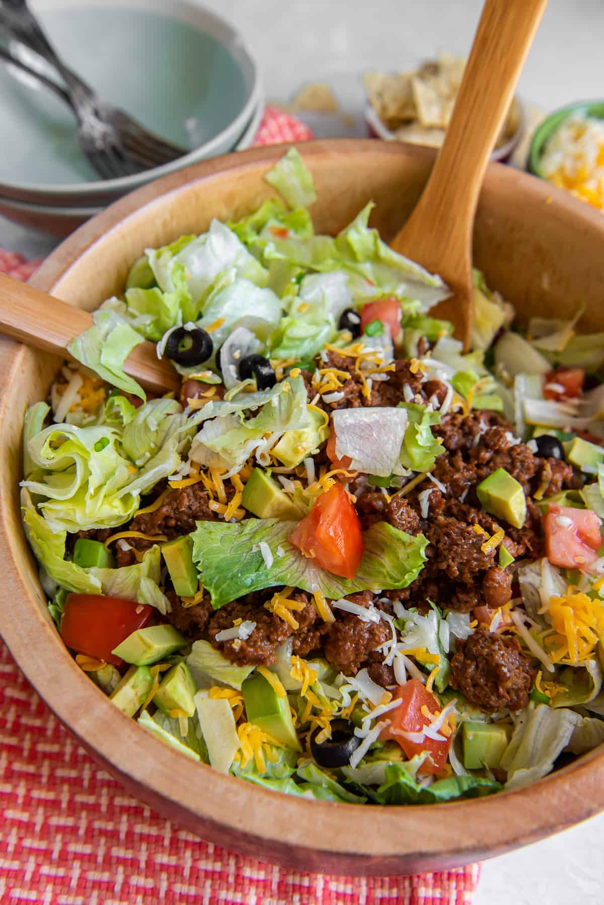 Wood salad spoons resting in a bowl of taco salad.