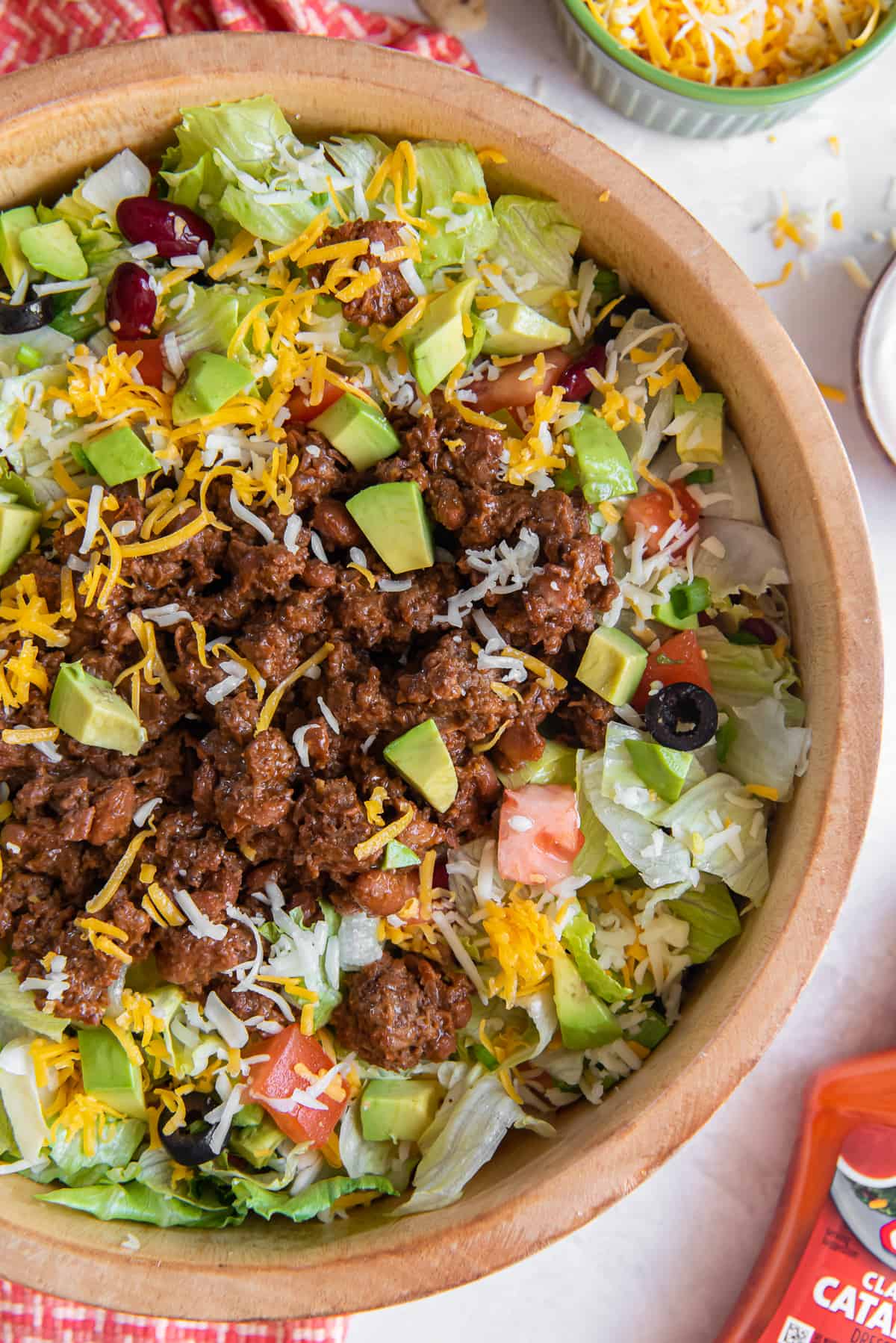 A top down shot of taco salad in a wood salad bowl next to a bottle of Catalina dressing.