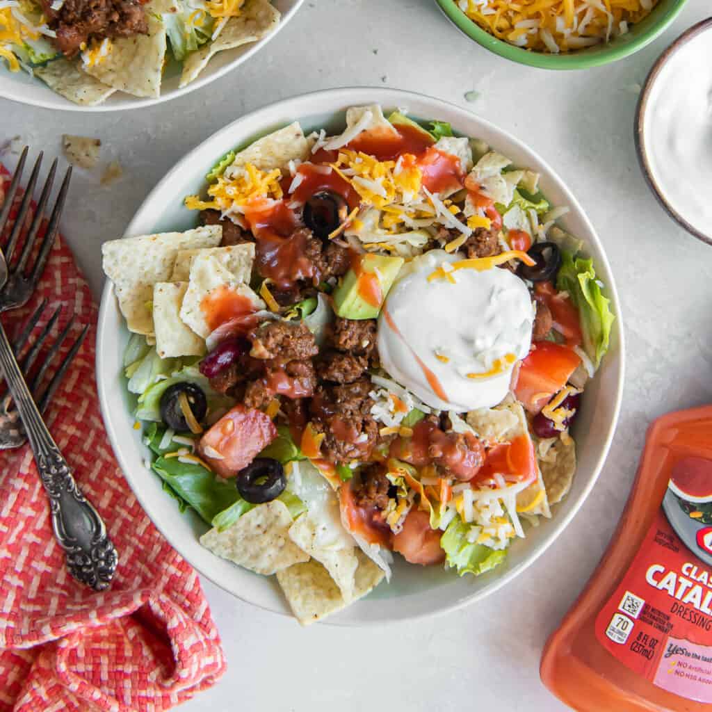 Two bowls of taco salad topped with Catalina dressing and sour cream.