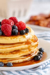 A stack of pancakes topped with fresh berries and maple syrup on a white plate.